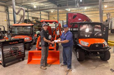A man is giving documents to a Chemeketa Diesel Technology student in front of Kubota branded equipment. The two are shaking hands. The implication is the man is giving the student paperwork to start a job after their completion of the Diesel Technology program.